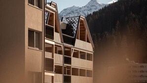 Un immeuble à plusieurs étages doté d’un toit à pente, de grandes fenêtres et offrant une vue sur une montagne enneigée.