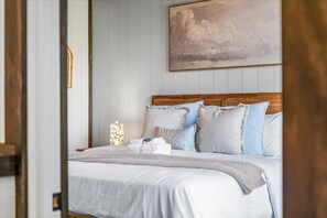 A neatly made bed with a wooden headboard, a bedside lamp, and a painting of clouds on the wall. - Cozy 2-bedroom cabin in perfect Sevierville with AC (Sevierville)