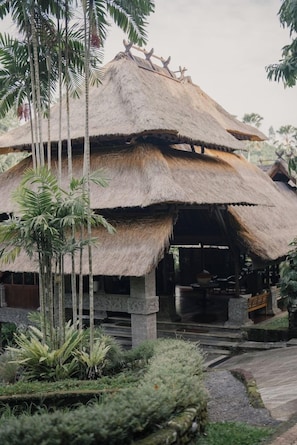 A thatched-roof structure with a covered entrance, surrounded by tropical vegetation.
