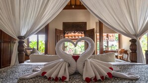 A bedroom with a canopy bed, a heart-shaped towel arrangement, and a view of the outdoors.