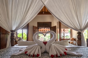 A bedroom with a canopy bed, a heart-shaped towel arrangement, and a view of the outdoors.