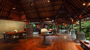 A spacious indoor area with a high ceiling, wooden flooring, and a central seating area with a round table and chairs.