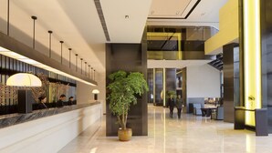 Un hall d’hôtel moderne avec un comptoir d’accueil, une grande plante en pot et un escalier menant à un étage supérieur.