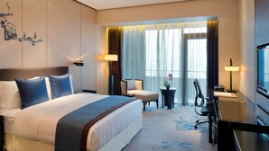Une chambre d’hôtel avec un grand lit, un bureau, une chaise, une télévision et une fenêtre avec des rideaux.