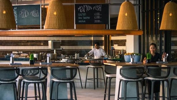 A restaurant with a bar area, bar stools, and a chalkboard menu listing items like salmon and red snapper.