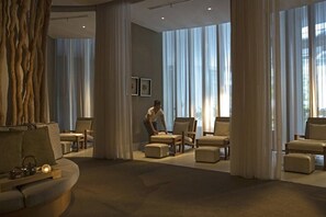 A modern hotel lobby with a sofa, chairs, and a person arranging furniture. - The Stones Hotel Legian Bali Autograph Collection (Legian)