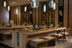 A modern bar area with wooden furniture, hanging pendant lights, and a long counter with glasses and bottles. - The Stones Hotel Legian Bali Autograph Collection (Legian)