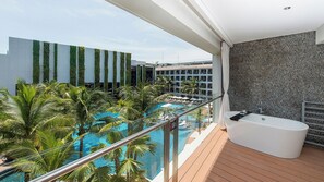 A balcony with a view of a swimming pool, a jacuzzi, and a modern building with vertical gardens. - The Stones Hotel Legian Bali Autograph Collection (Legian)