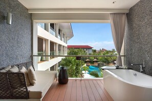 A balcony with a view of a swimming pool, a bathtub, and a lounge area with a sofa and a coffee table. - The Stones Hotel Legian Bali Autograph Collection (Legian)