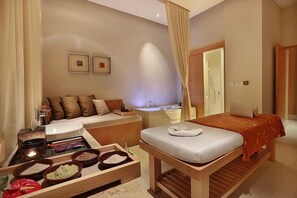 A hotel room with a bed, a sofa, a massage table, a small table with bowls, and a bathroom with a bathtub and sink. - The Stones Hotel Legian Bali Autograph Collection (Legian)
