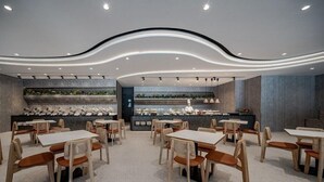 A modern restaurant interior with multiple dining tables and chairs, a counter with a display of food items, and a curved ceiling design. - Guan Xiang Century Hot Spring Hotel (Jiaoxi)