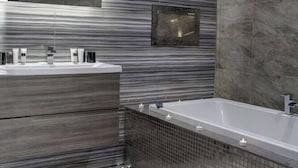Un baño moderno con una bañera grande, un tocador con espejo y una pared con textura.