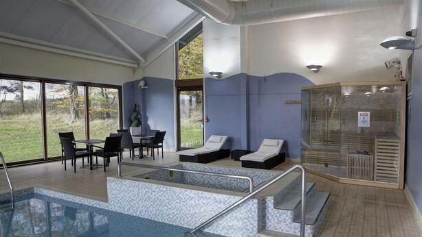 Una piscina interior con sillones de descanso, una mesa y sillas.