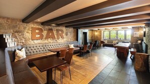 Una zona de bar con pared de piedra, vigas de madera en el techo y un conjunto de asientos.