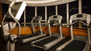 Ett gym med löpband och en roddmaskin, stora fönster med utsikt över staden om natten.