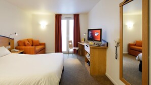 Habitación de hotel con una cama, un escritorio con una computadora, una silla y un espejo grande.