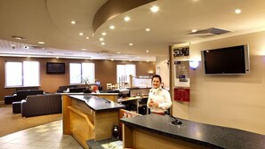 Zona de recepción de hotel con mostrador, asientos y televisor.