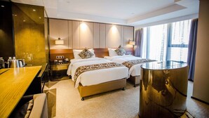 Una habitación de hotel con cama, mesitas de noche, un escritorio y un ventanal grande.