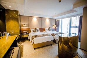 Una habitación de hotel con cama doble, mesitas de noche, un escritorio y una mesa de vidrio.