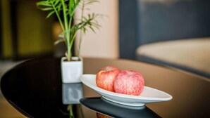 Una mesa de comedor con un plato blanco que sostiene dos manzanas, una planta en maceta y un sofá moderno al fondo.