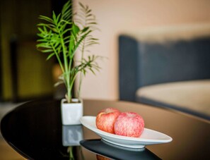 A dining table with a white plate holding two apples, a potted plant, and a modern sofa in the background. - Park Hotel Xiamen (Xiamen)