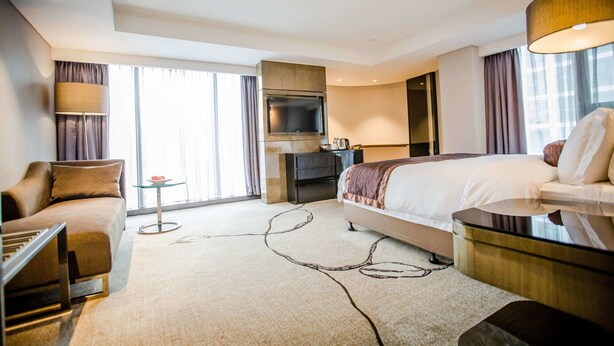 Habitación de hotel con cama, escritorio, televisor, sofá y lámpara.