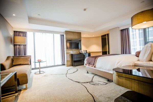 Una habitación de hotel moderna con una cama grande, un escritorio, un televisor y una zona de estar.