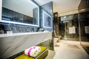 Un baño moderno con tocador de mármol, un espejo grande y cabina de ducha con mampara de vidrio.