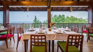 Ein Restaurant mit gedeckten Tischen, gepolsterten Stühlen und Blick auf das Meer.