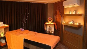 Un cuarto de masajes con una camilla, una mesita con un adorno y un estante con artículos de tocador.