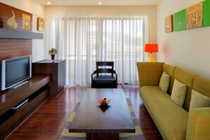 Una sala de estar moderna con un televisor de pantalla plana, una mesa de centro de madera con fruta, un sofá verde y una silla negra.