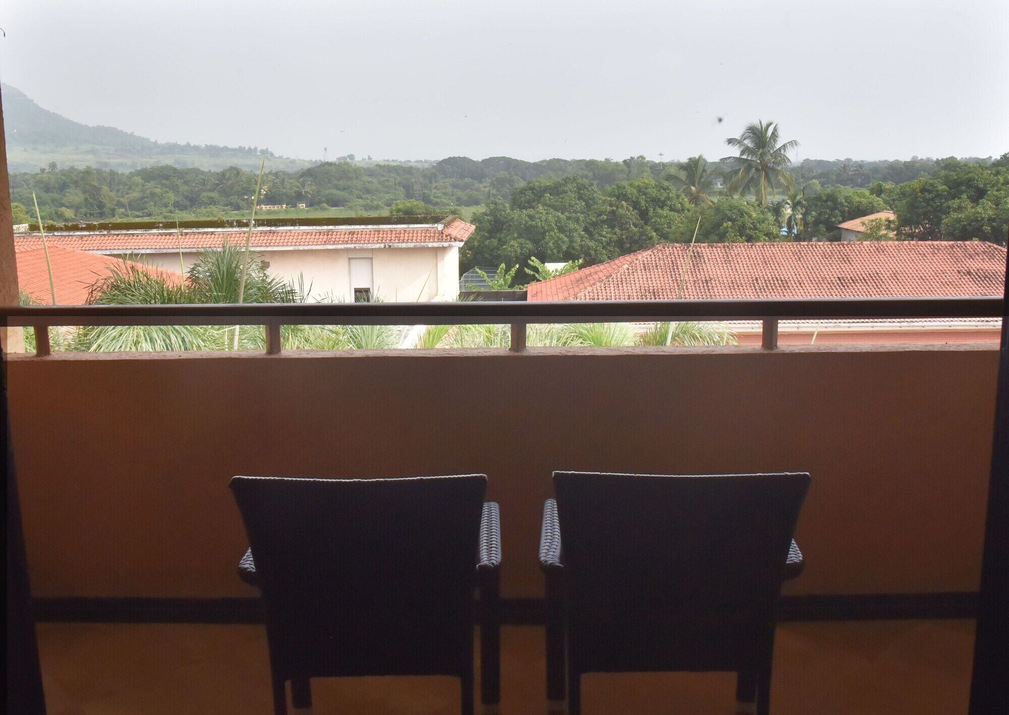 Ein Balkon mit zwei Stühlen, der auf einen Wohnbereich mit Häusern und Palmen blickt.