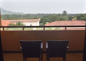 A balcony with two chairs facing a view of a residential area with houses and palm trees. - Taj Alibaug Resort & Spa, Maharashtra (Alibag)