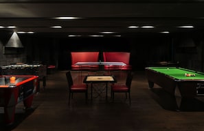 Una sala poc il·luminada amb billar, seients vermells i taula de futbolí.