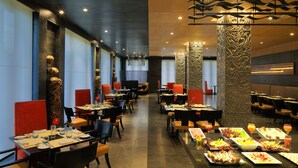 A modern dining area with multiple tables and chairs, decorative columns, and a variety of food items displayed on the tables. - Taj Alibaug Resort & Spa, Maharashtra (Alibag)