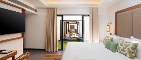 A hotel room with a large bed, a desk with a chair, a television, and a view of the outdoor seating area.