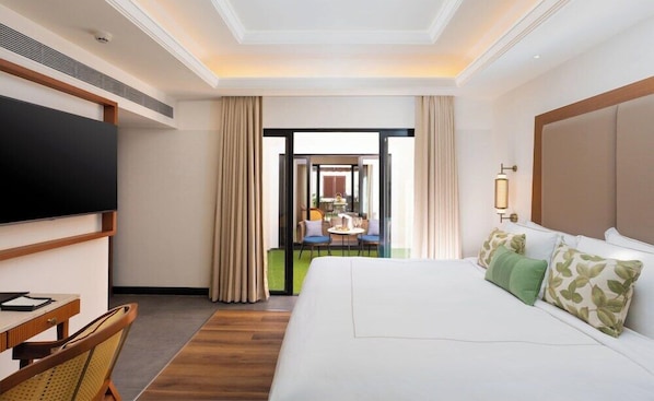 A hotel room with a large bed, a desk with a chair, a television, and a view of the outdoor seating area. - Taj Alibaug Resort & Spa, Maharashtra (Alibag)