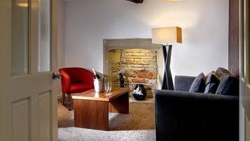 A cozy living room with a stone fireplace, a red armchair, a grey sofa, and a wooden coffee table with a bottle of champagne and glasses.