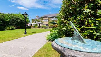 A pathway leading to a stone building with a garden and a sundial.