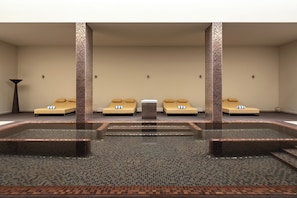 Un espace spa comprenant un grand bain à remous central, quatre chaises longues beiges et un sol carrelé.
