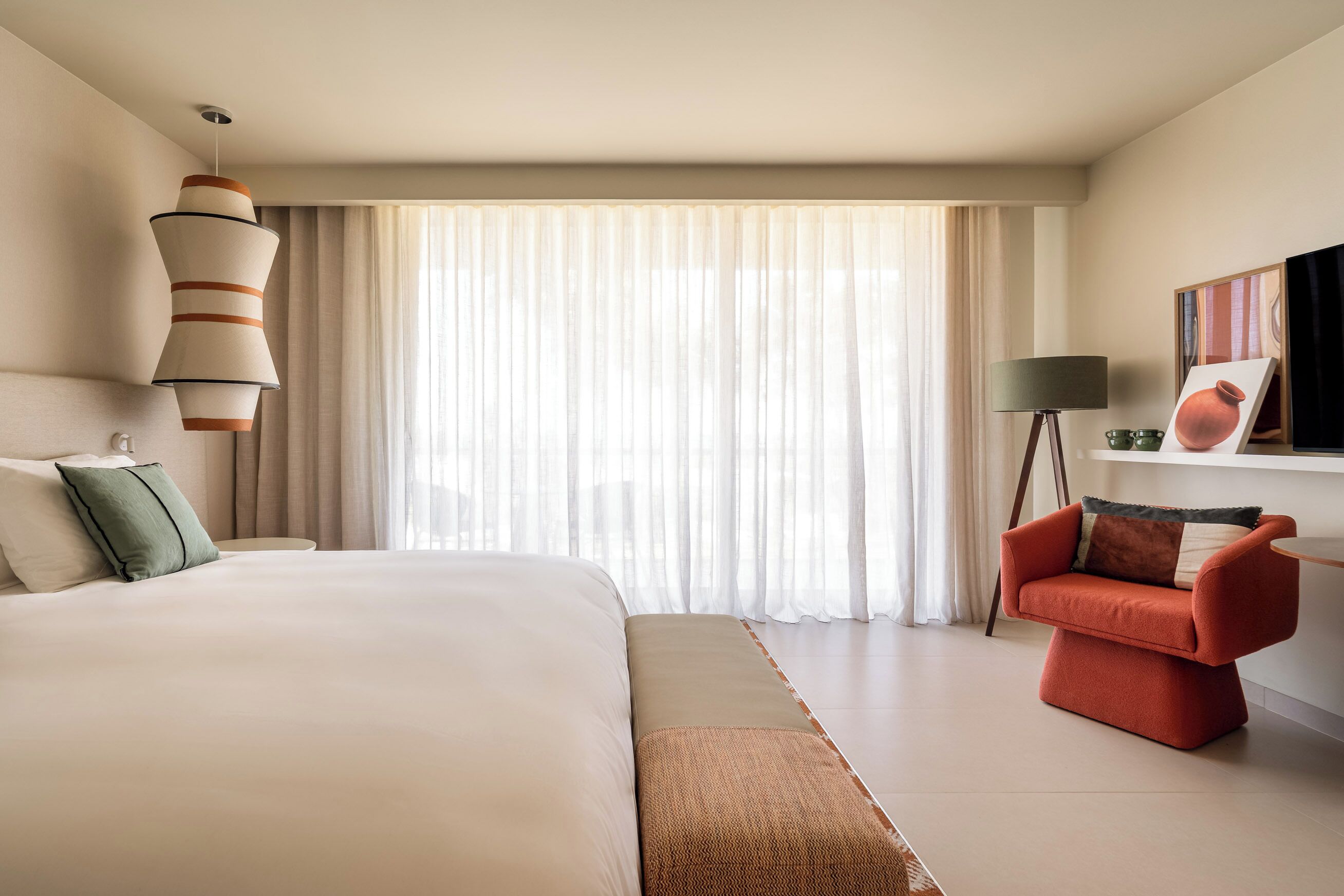 Een moderne hotelkamer met een groot bed, een rode fauteuil, een staande lamp en een schilderij aan de muur.