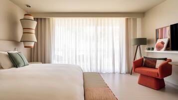 A modern hotel room with a large bed, a red armchair, a standing lamp, and a painting on the wall.