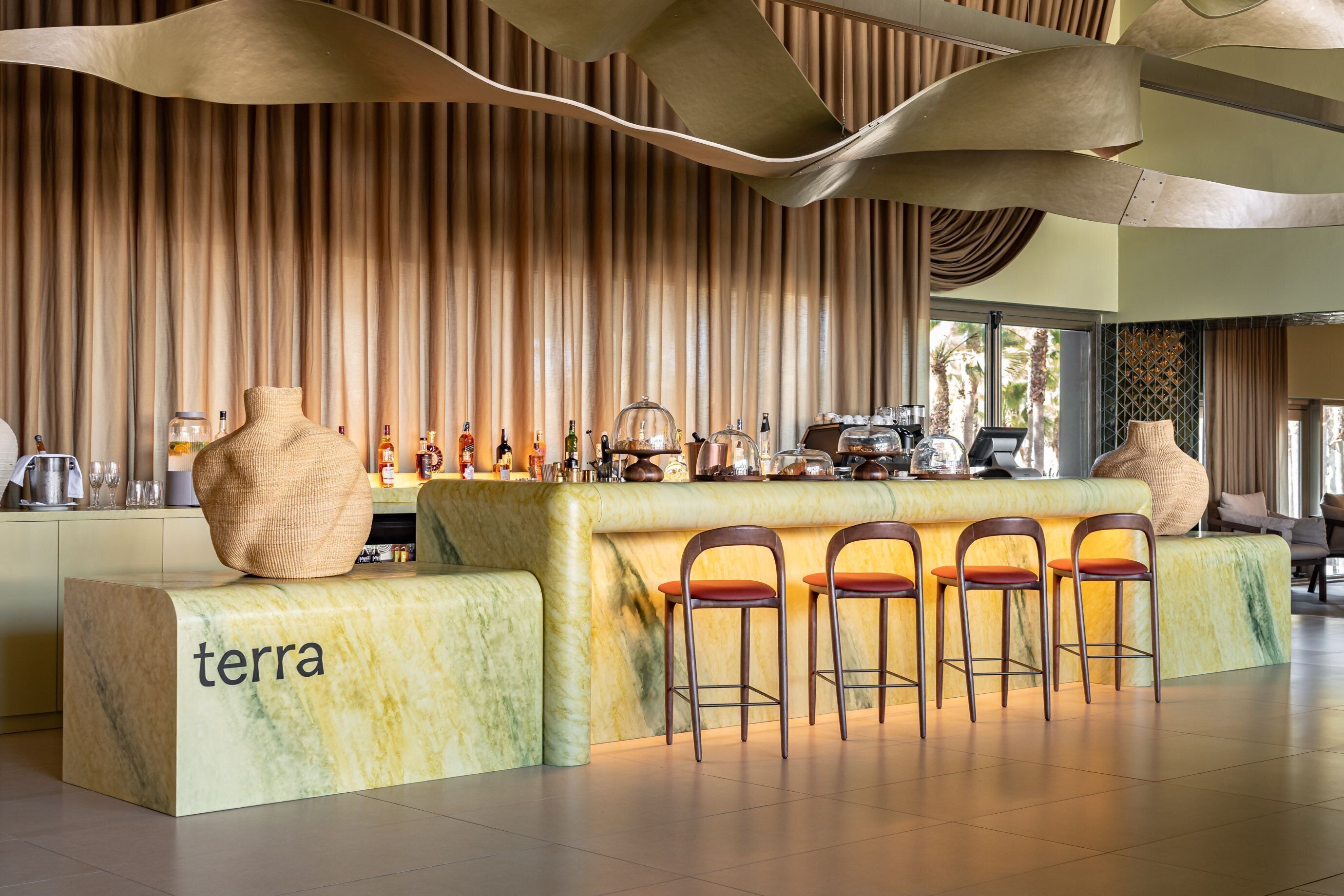 Uma área de bar com balcão de mármore, banquetas e um vaso grande.