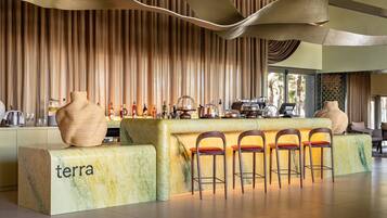 Uma área de bar com balcão de mármore, banquetas e um vaso grande.
