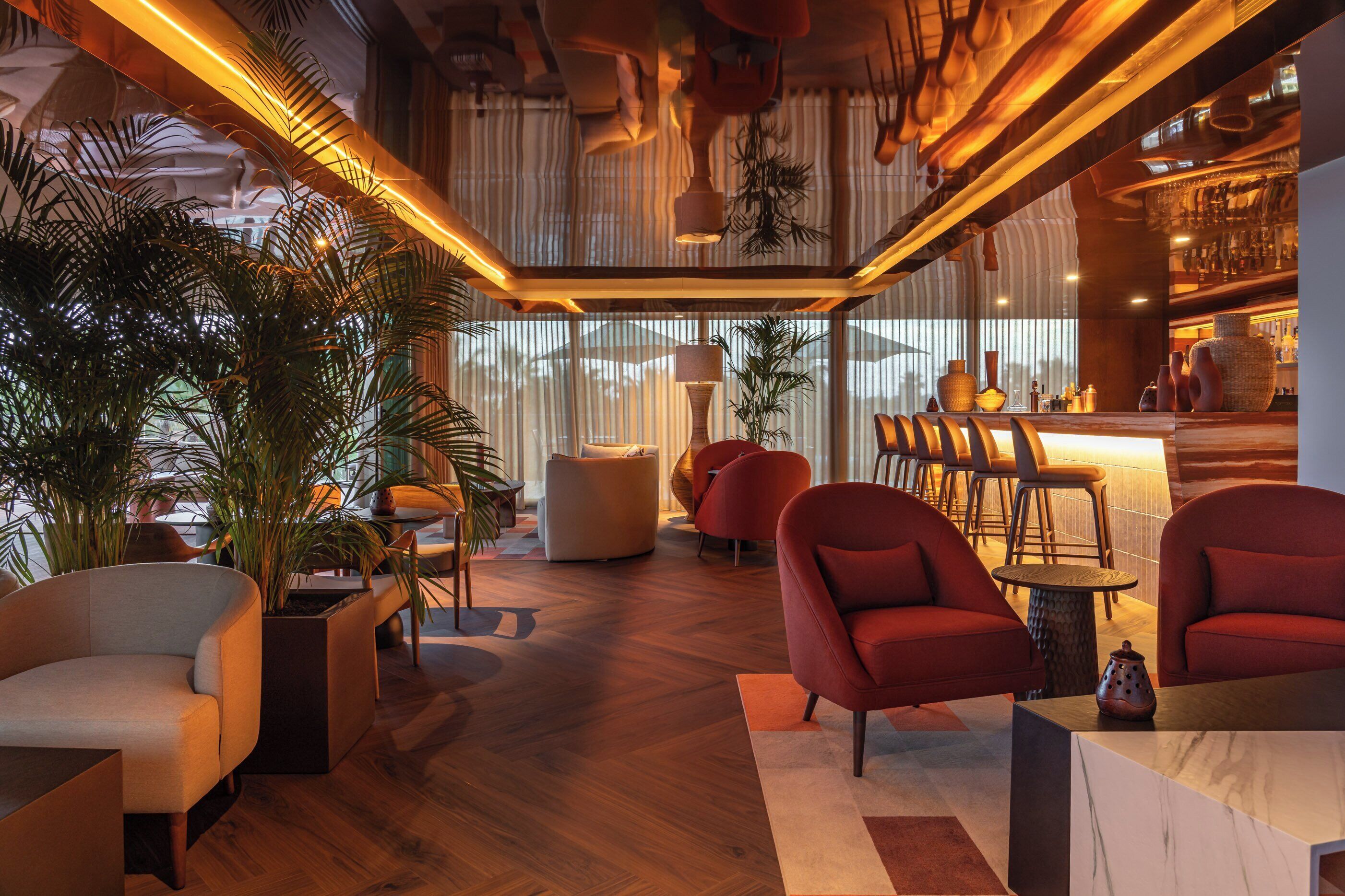Een moderne loungeruimte met houten vloer, rode en witte meubels en grote ramen voor natuurlijk licht.