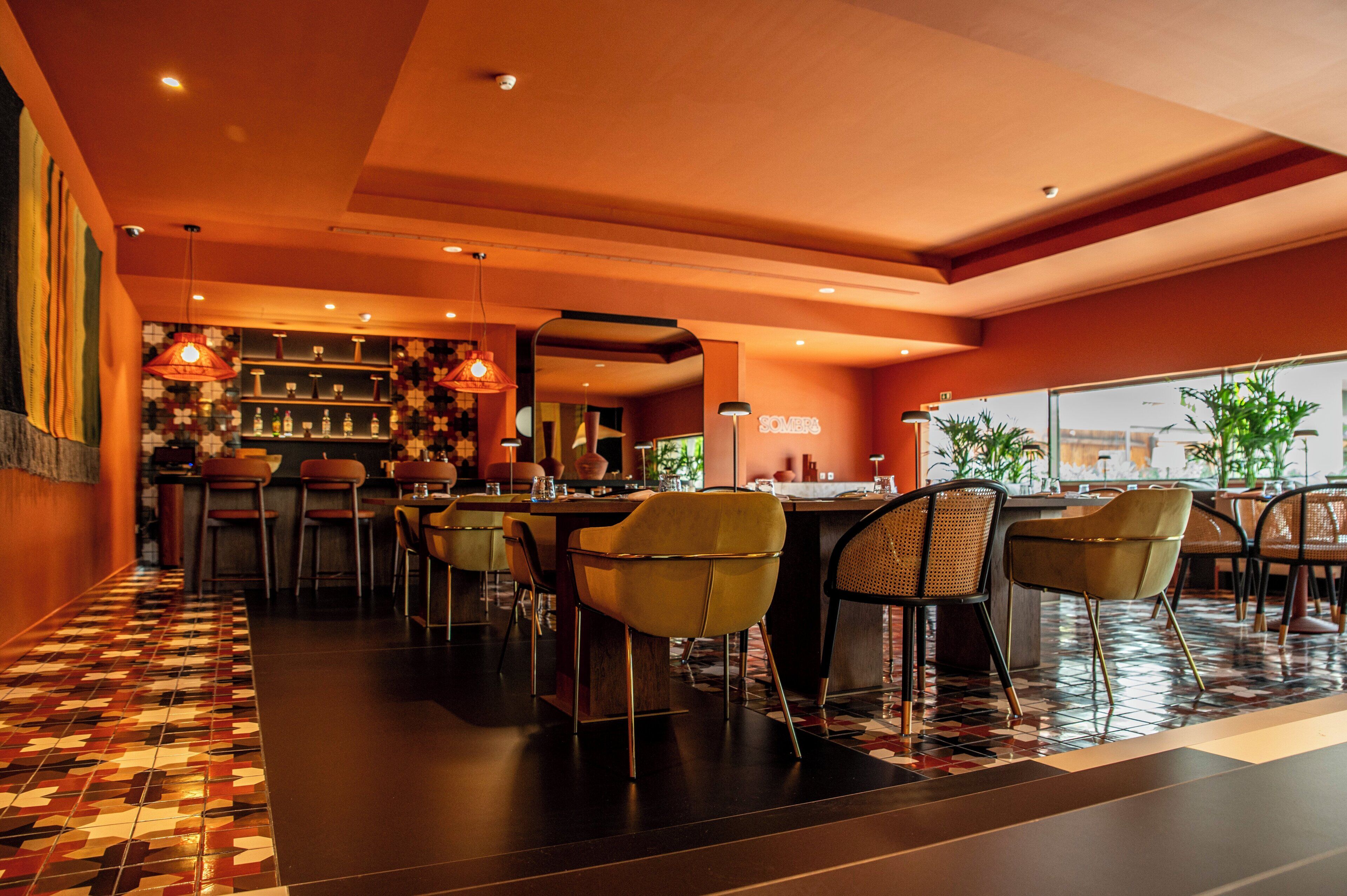 Een restaurant met een bar, verschillende zitmogelijkheden waaronder barkrukken en stoelen, en een vloer met een patroon.