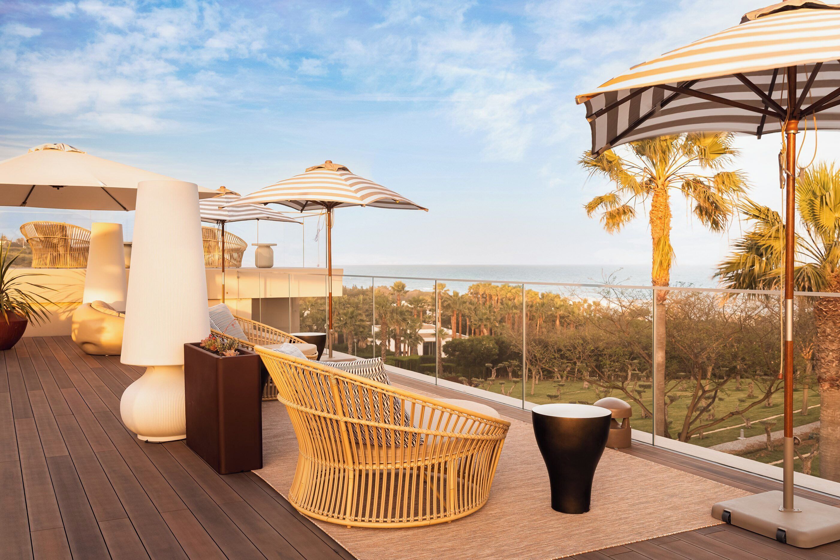Een balkon met rieten meubilair, grote parasols en uitzicht op de oceaan.