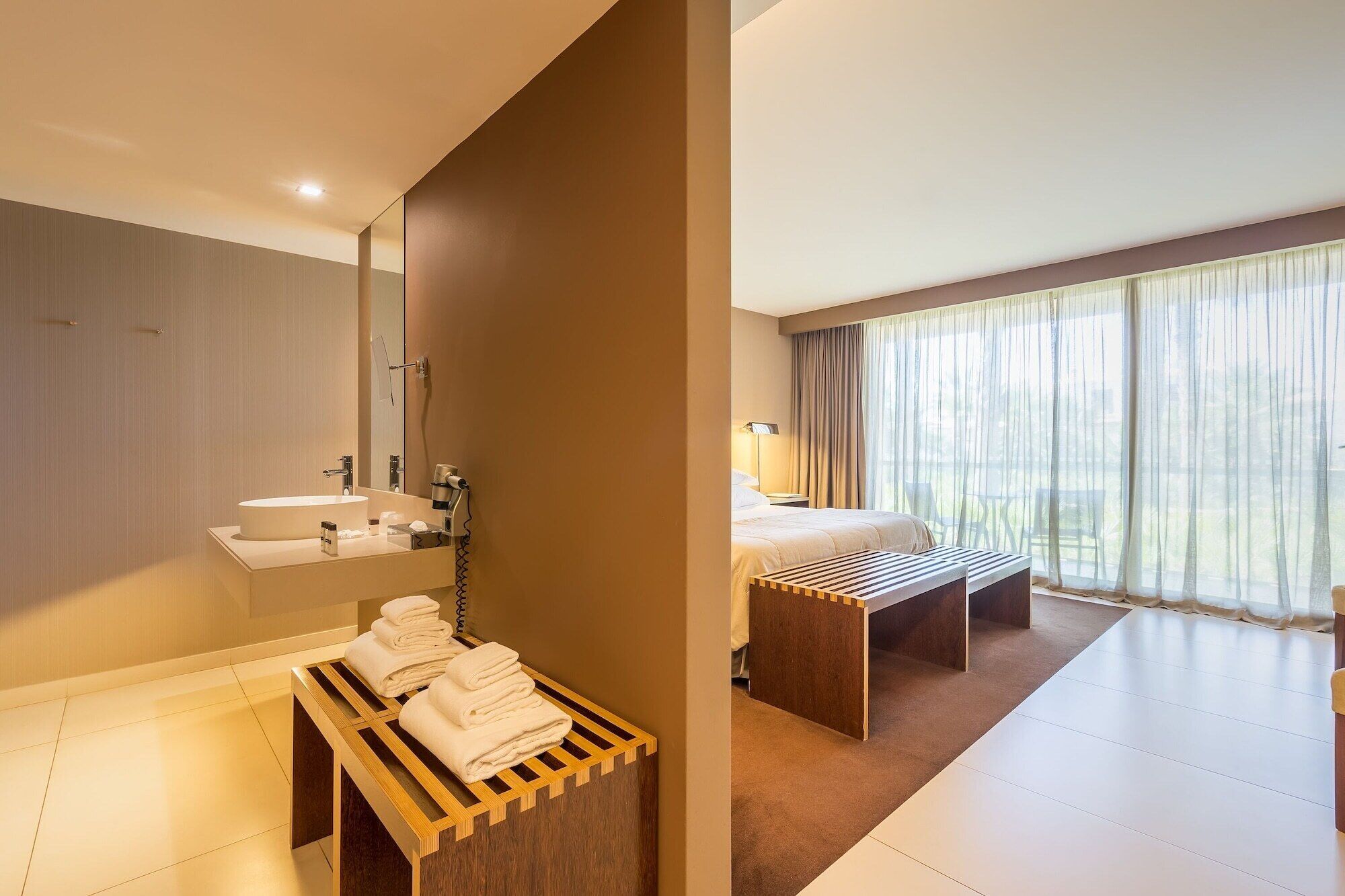 Een hotelkamer met een badkamer, een bed, een nachtkastje en een raam met gordijnen.