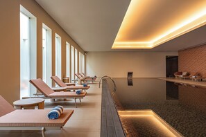 Un área de spa con tumbonas, piscina y mostrador de recepción.