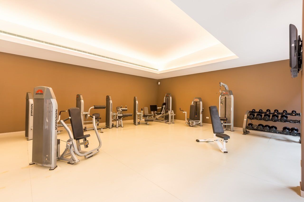 Uma academia com diversos equipamentos de exercício, um banco e uma estrutura com halteres.